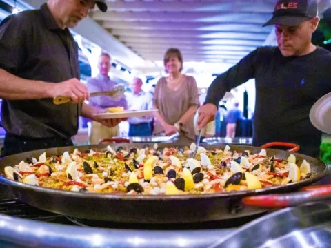 Chefs serving seafood paella to guests at an evening event