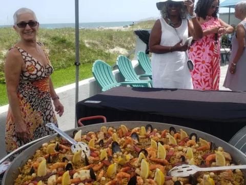 Guest smiling beside a pan of seafood paella at a beach house party