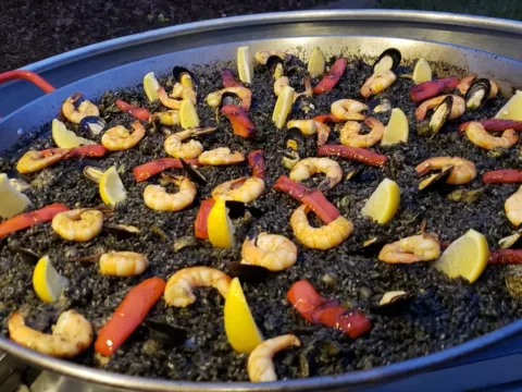 Black paella with shrimp and lemon wedges in a large pan