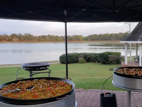 Two paella pans cooking on a patio beside a lake