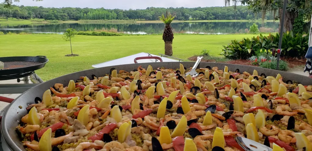 Giant seafood paella cooking on a lawn overlooking a lake