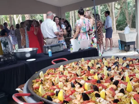 Guests gathered around a pan of seafood paella at a covered pavilion