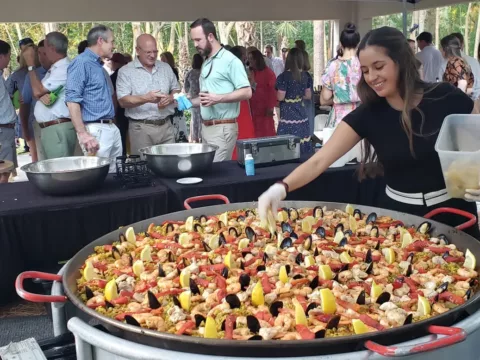 Server garnishing a pan of seafood paella at an outdoor reception