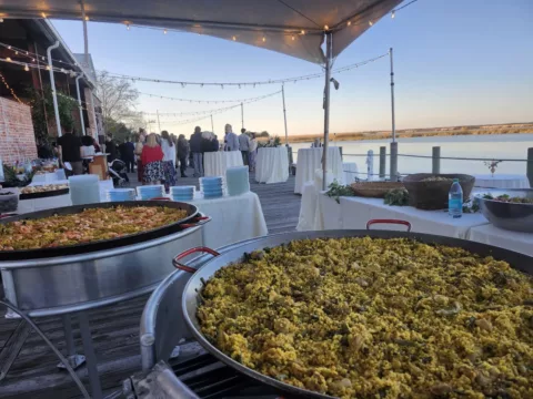 Two paella pans cooking on a waterfront deck at an evening wedding