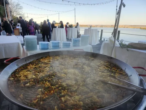 Paella simmering as wedding guests gather on a waterfront deck